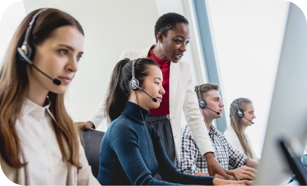 A row of customer service representatives talk on the phone while another person stands behind one and talks to them