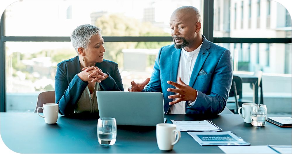 Woman and man sitting at conference table reviewing information on an open laptop computer.