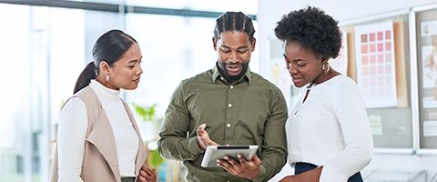 Three individuals engaged in discussion while viewing information on a tablet computer together