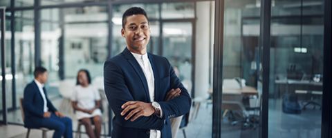 Person in business casual attire standing in an office setting smiling with crossed arms.