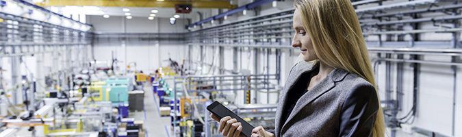 Business woman overlooking factory floor with tablet device