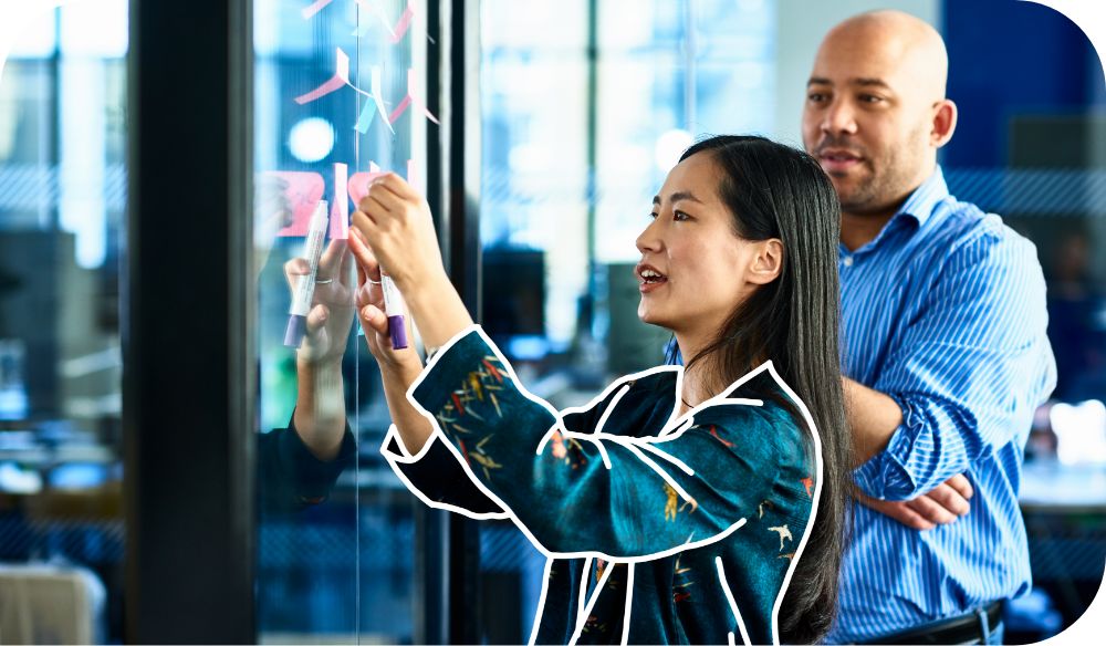 Woman holding up notes for coworker standing behind her to review. 