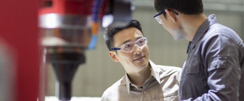 Two people in safety glasses with tablet at manufacturing station
