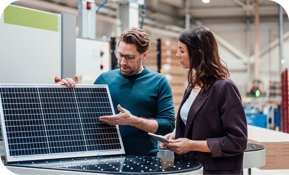 Two businesspeople stand together, having a discussion over a display in a warehouse setting