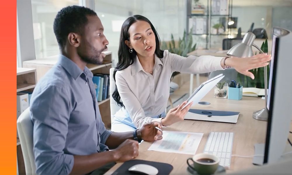 A woman and a man look at a computer monitor and discuss what they see onscreen.