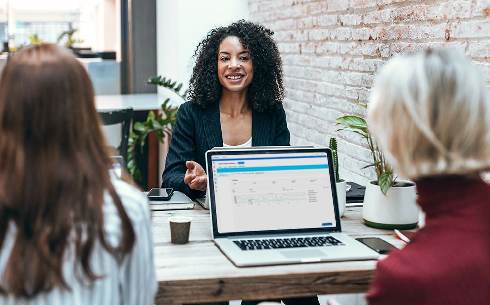 Three women sit at a table with a laptop. 