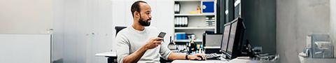 A person holds a phone while working at a computer in an office environment