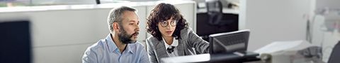 A person points at a computer screen in an office while another person looks on