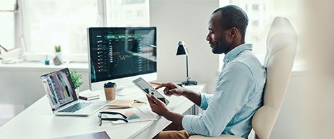 A person works at a desk with a computer monitor while holding a tablet