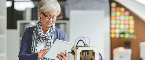 Woman in a blue sweater and scarf sitting while working on a tablet device