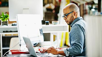 Side view of a man while he sits at a desk in an office area and works on a laptop device