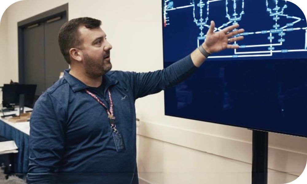 Businessperson gives presentation while motioning towards a diagram on a television screen.