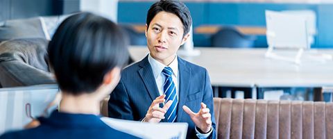 A person in a business suit sitting at a table talking to others.