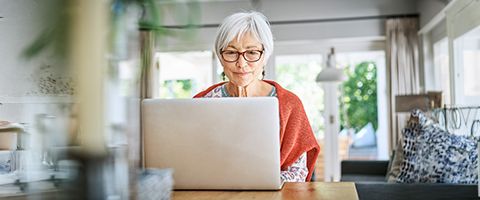 Person in a home setting sitting at a table looking at a laptop.