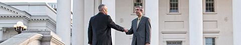 Two people in business attire standing outside a government building shaking hands.