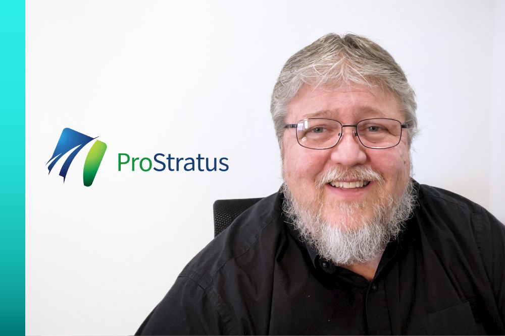 Person in a black button-up shirt and glasses smiling next to the blue and green ProStratus text logo.