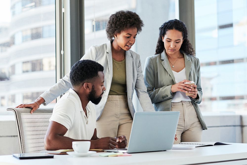 Three businesspeople look at a laptop screen together. 