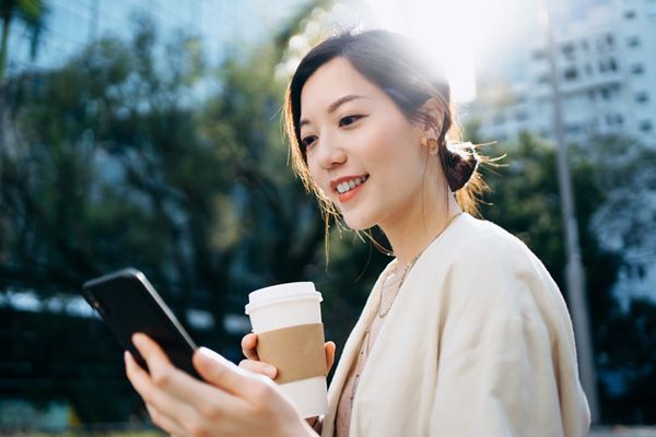 Woman holding coffee cup outside looking at her cell phone 