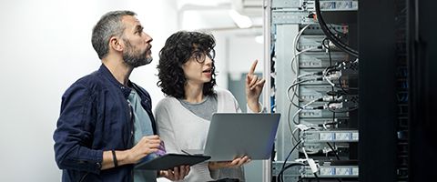 Two professionals working on server maintenance in a data center, with one using a laptop as the other observes.