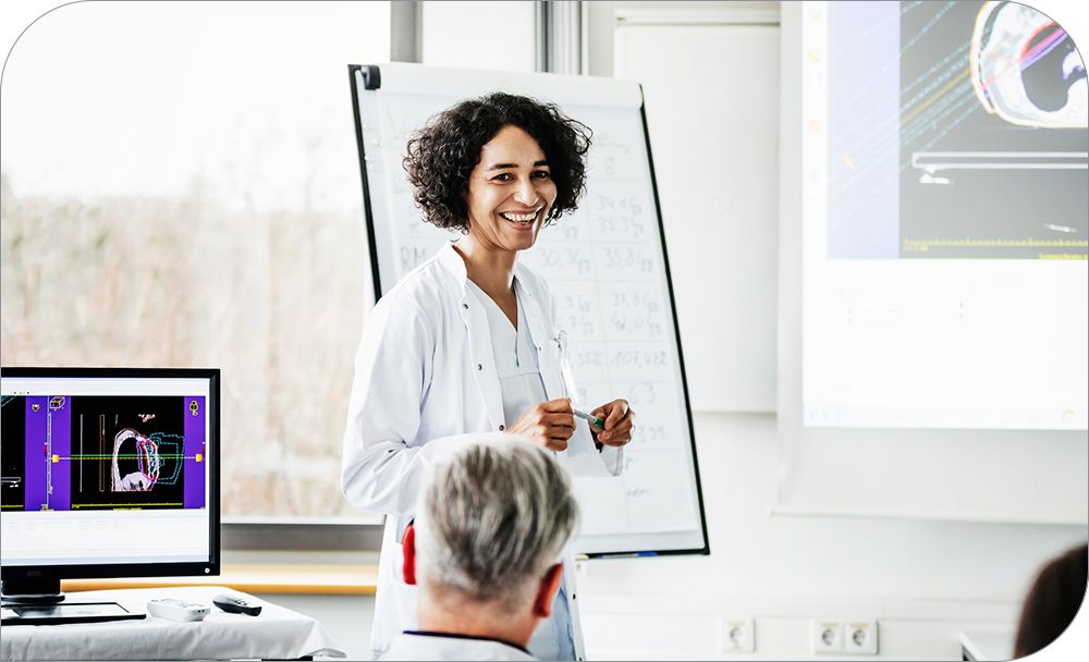 A clinical doctor smiles while she gives an informational talk to a group inside a hospital  