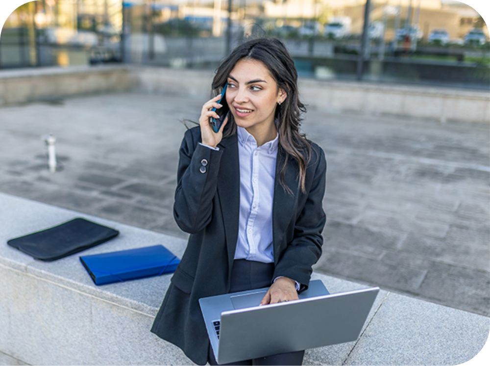 Professional woman outside of an office building holding a laptop and talking on her mobile phone