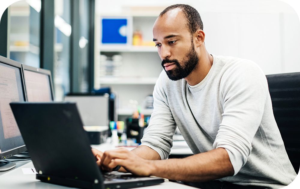 Man in a white shirt sitting at a desk while working on a laptop device