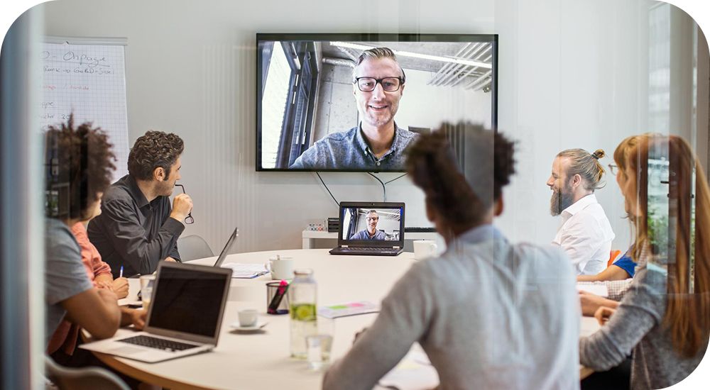 Employees sitting at a table looking at a colleague on a video call.