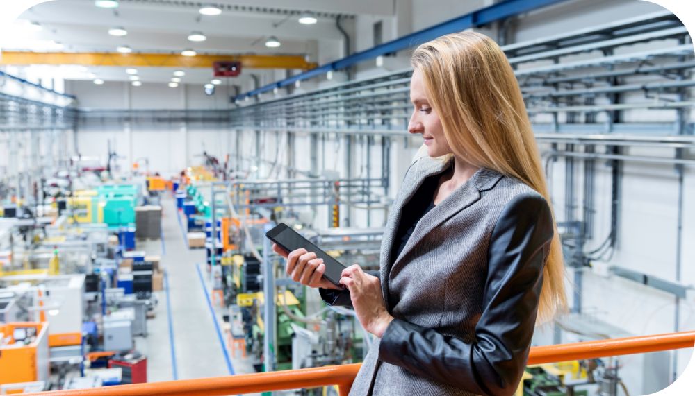 Business woman standing above a factory floor in a warehouse while working on a tablet