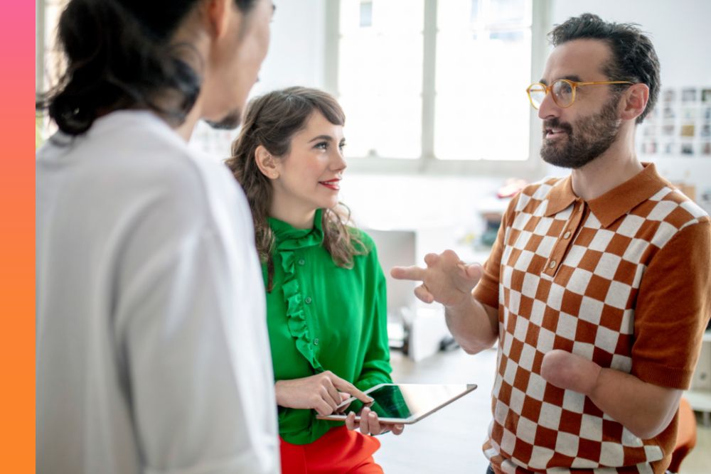 Man in a brown and white checkered sweater while talking to a woman in a green shirt and another person across from him