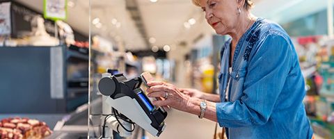 A person in a jean button-up uses their phone at a store to make a purchase in a check-out line