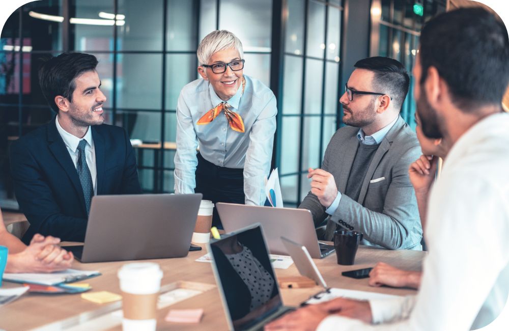 A group of people chat at a table while working on laptop computers.