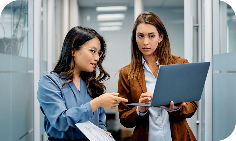 Two businesspeople standing together and discussing something on the laptop that the one on the right is holding