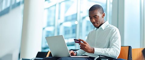 A person in a white button-up shirt works on a laptop and looks at their payment card.