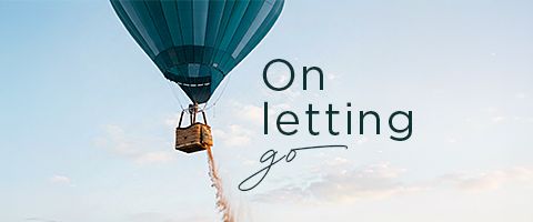 A teal hot air balloon floats in a clear sky, with its basket suspended and sand or ballast pouring out. The scene is set against a soft, pastel horizon, creating a calm and uplifting atmosphere. Overlay text reads "On letting go" in a clean, modern typeface. The overall visual suggests freedom, release, and emotional transformation.