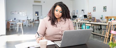 モダンなオフィススペースでラップトップを使い、紙に何かを書いている女性