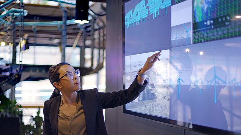 Woman pointing at touchscreen monitor displaying four images of wind turbines 
