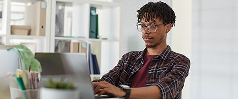 Person in casual attire sitting at a desk using a laptop.