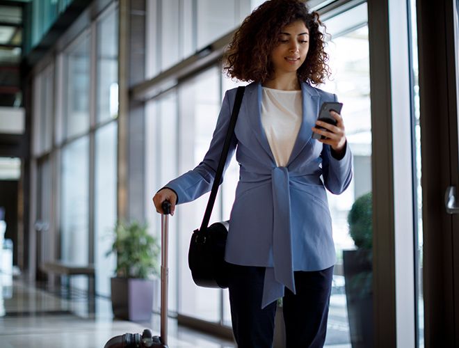 Business woman standing next to her luggage while looking at her phone