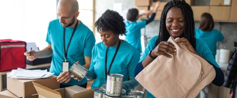 People in matching teal t-shirts volunteer together preparing and boxing food at a relief organization