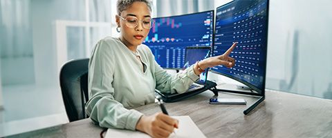 Customer support analyst viewing three monitors of data on a desk in a operations room.