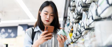A shopper looks at her phone while holding an item from the store for consideration
