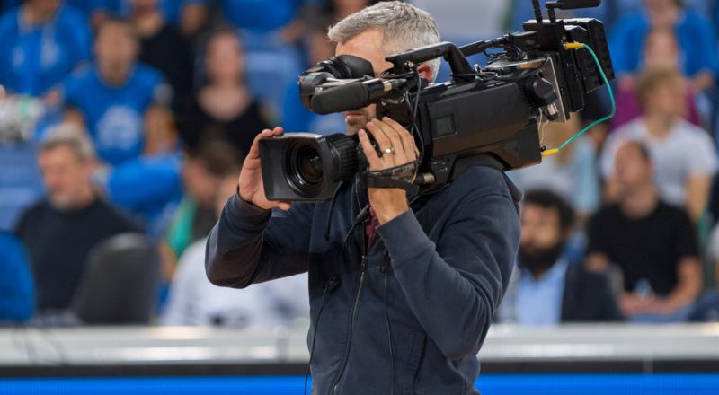 Man holding a video camera in front of an out of focus crowd