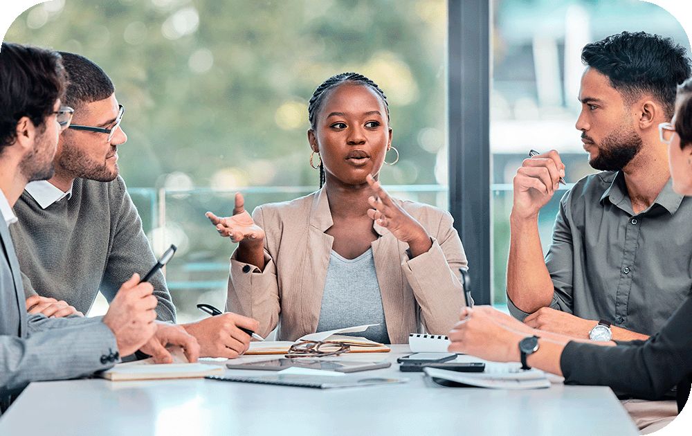  Female co-worker seated at head of conference table discussing action plans with colleagues on either side