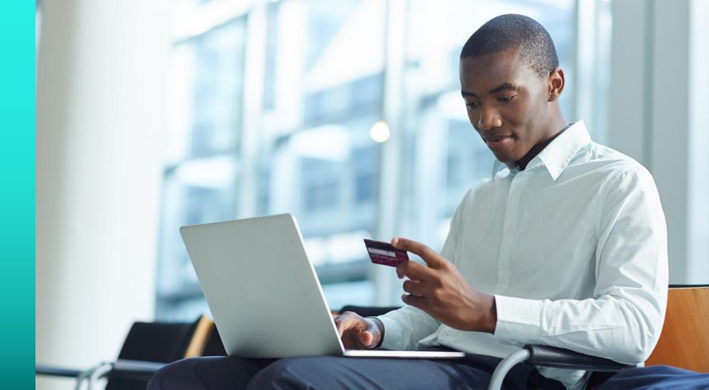 Individual with portable computer open on their lap typing in credit card information on the computer keyboard. 