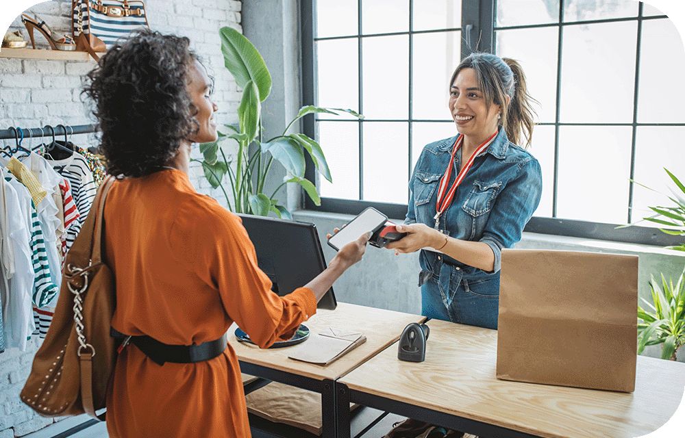 A retail store worker helps a customer pay with their phone at a table.