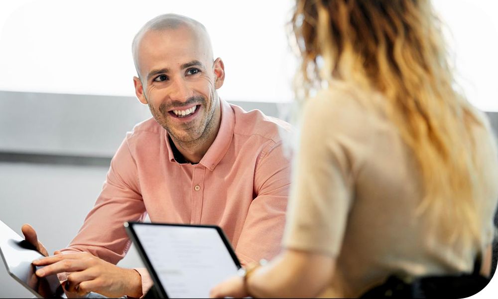 Two businesspeople converse while working from tablets 