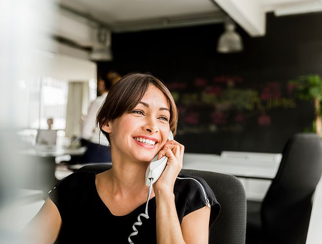 Business woman sitting at a desk in a brightly lit office space while talking on the phone