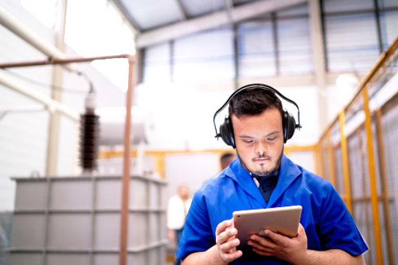 A person wearing headphones walks through a warehouse while looking at a tablet