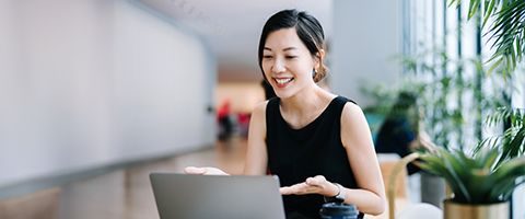 Woman sitting at a desk next to plants while gesturing at her laptop device