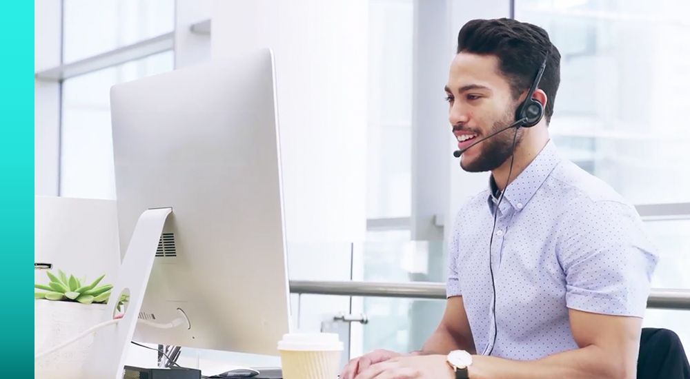 Person sitting at a desk and working on a desktop monitor while talking on a headset